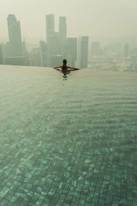 Rear view of woman in infinity pool against skyscrapers