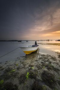 Boat moored on shore against sky during sunset