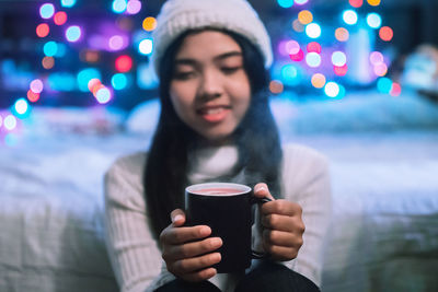 Young woman having coffee against illuminated lights