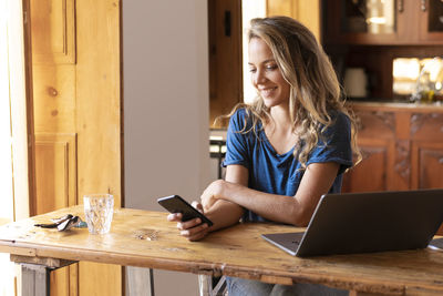 Young woman using phone while sitting on table