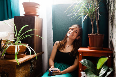 Woman looking away while sitting on potted plant at home