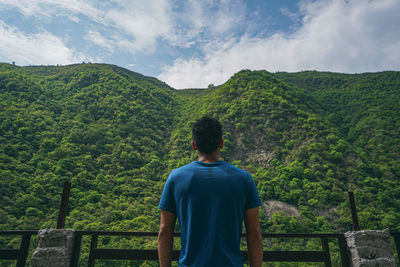 Young indian boy standing in the edge of the balcony, enjoying the scenic view of the green mountain