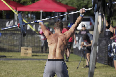 Rear view of disabled shirtless man lifting deadlift while standing at park