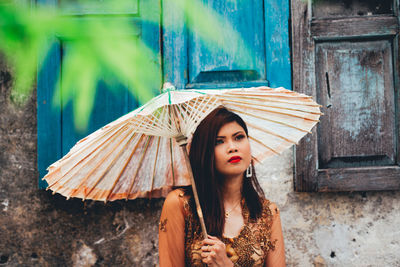 Woman with umbrella standing on street against building