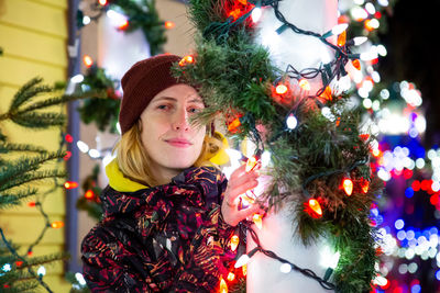 Portrait of young woman standing by christmas decorations at entrance