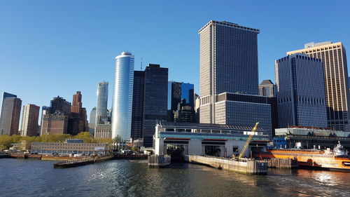 Modern buildings by river against clear sky in city