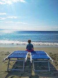 Rear view of child sitting on seat at beach against sky