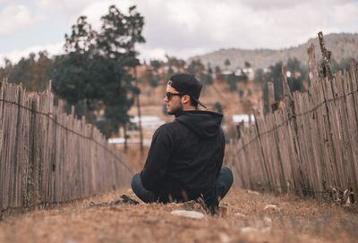 Rear view of young man sitting on land against sky