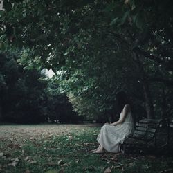 Side view of woman wearing dress while sitting on bench at park