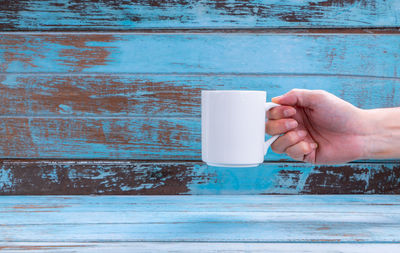 Midsection of person holding coffee cup against wall