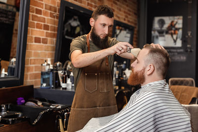 Hairdresser cleaning man's face using brush at salon