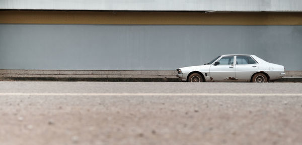 An old, broken car parked next to an advertising space and a foreground, blurry road