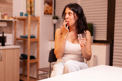 Young woman using phone while sitting on bed at home