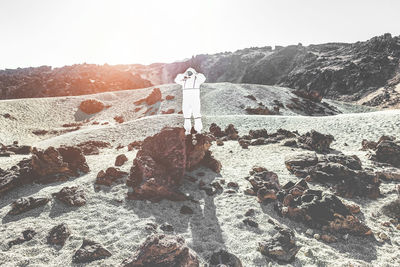 Astronaut standing on rock against sky