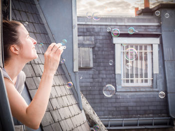 Side view of woman blowing bubbles from window