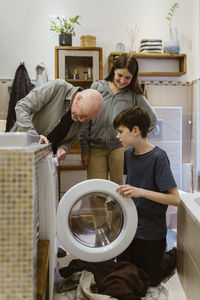 Senior man assisting grandchildren while doing laundry in bathroom at home