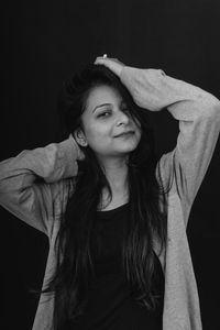 Portrait of young woman standing against black background