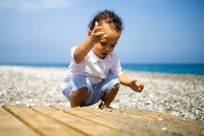 Happy kid in white shirt and blue shorts plays with pebble on the beach