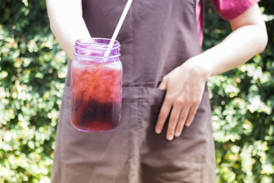 Midsection of woman holding drink in jar outdoors