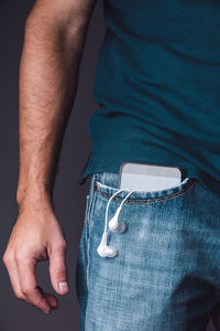 Midsection of man with mobile phone and in-ear headphones in pocket