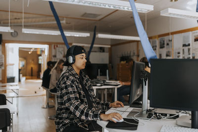 Young man using computer while listening through headphones in lab