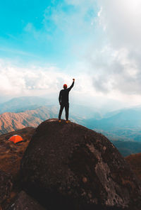 Rear view of man standing on rock against sky