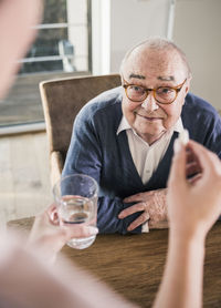 Woman holding pill and glass of water for smiling senior man