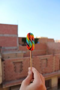 Cropped hand holding candy against building in city