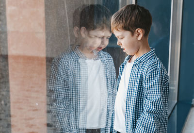 Boy in shirt looks out the window. reflection of a boy in the window. light and dark side