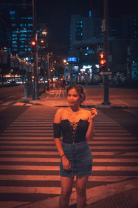 Full length portrait of young woman standing on road at night