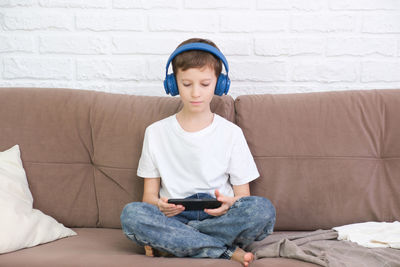 Portrait of young woman using phone while sitting on sofa at home