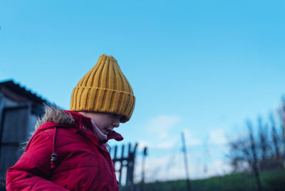 Relaxed, calm child in a red jacket and a yellow hat in nature against the sky. looking down. 