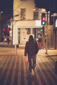 Rear view of man walking on footpath in city at night