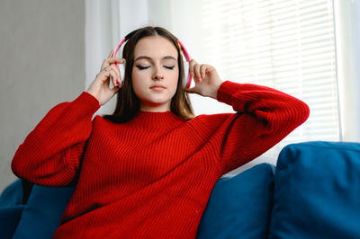 A young girl in a red  sweater works on a laptop at home. her cat and dog are sitting next to her