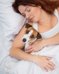 Portrait of young woman with dog on bed at home