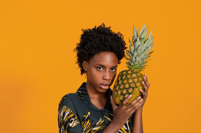 Young woman holding pineapple against yellow background