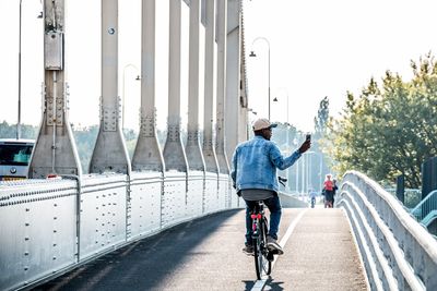Rear view of man riding bicycle on bridge in city