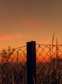 Close-up of chainlink fence against sky during sunset