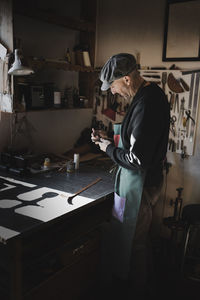 Craftsman using old gauge to measure thickness on brown leather in dark workshop