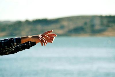 Close-up of hand against sea against sky