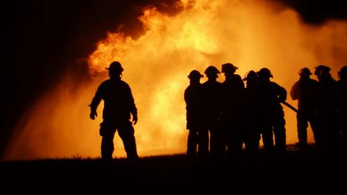 Silhouette people standing by fire at night