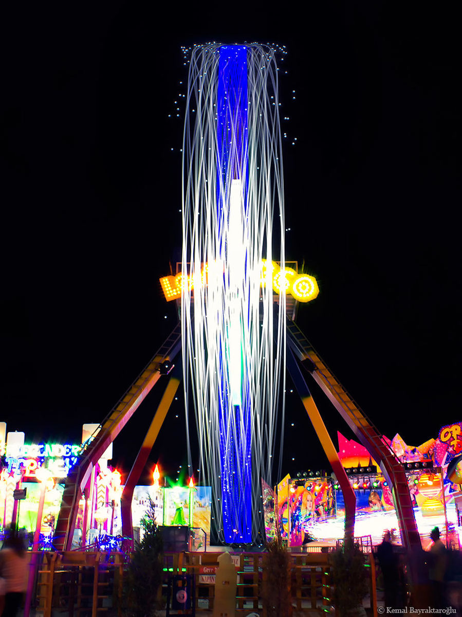 illuminated, night, low angle view, arts culture and entertainment, amusement park, built structure, amusement park ride, multi colored, architecture, lighting equipment, building exterior, long exposure, ferris wheel, carousel, clear sky, sky, famous place, travel destinations, blue, outdoors