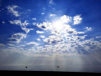 Low angle view of sunlight streaming through clouds over sea