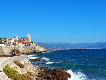 Scenic view of sea by buildings against clear blue sky