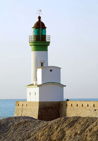 Lighthouse by sea against clear sky