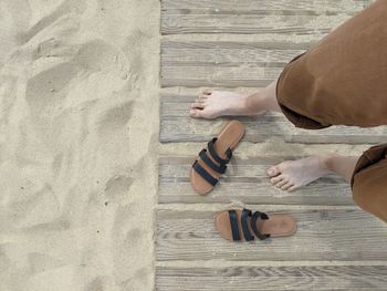 Personal perspective of looking down at bare feet with sandals on sand.