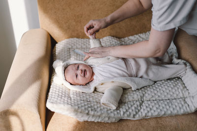 Mom dresses cute newborn little baby boy in a jumpsuit.
