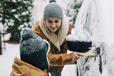 Son and mother clearing snow from car with scraper