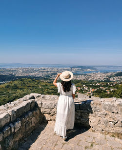 Rear view of woman standing on top of klis fortress overlooking coastal city of split in croatia.