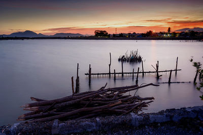 Wooden posts in lake against sky during sunset